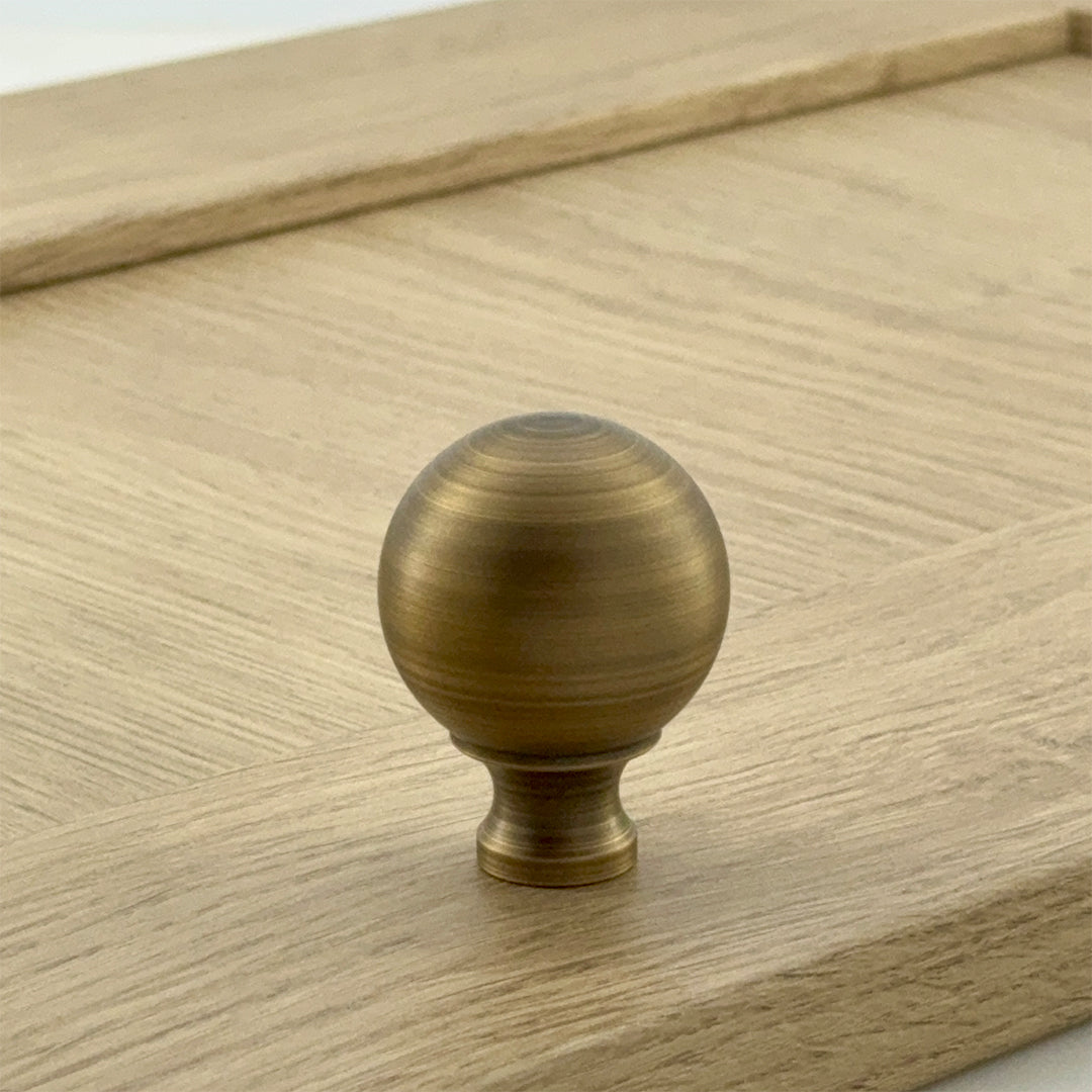 A gold-colored ball knob on a wooden surface, part of the Addington Collection.