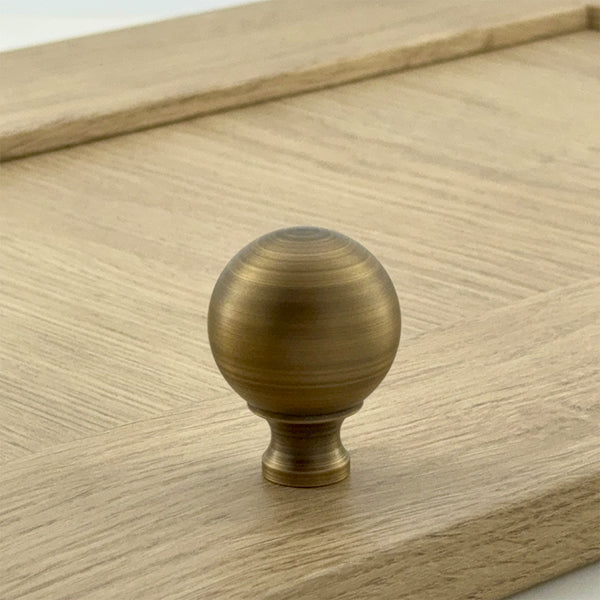 A gold-colored ball knob on a wooden surface, part of the Addington Collection.