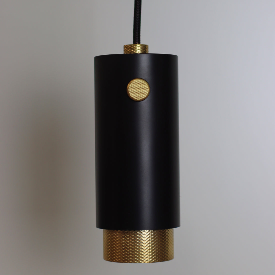pendant light from ceiling with fabric cable and solid brass accents. knurled brass. black cerakote paint light body. knurled decor. 