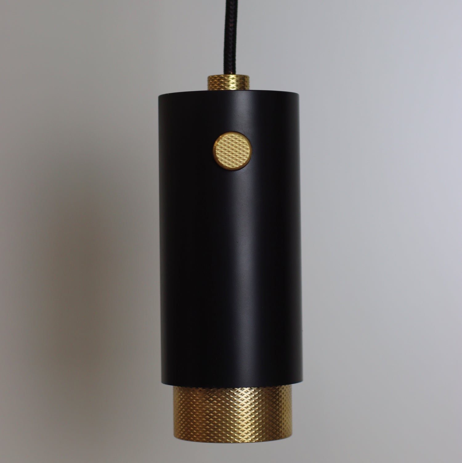 pendant light from ceiling with fabric cable and solid brass accents. knurled brass. black cerakote paint light body. knurled decor. 